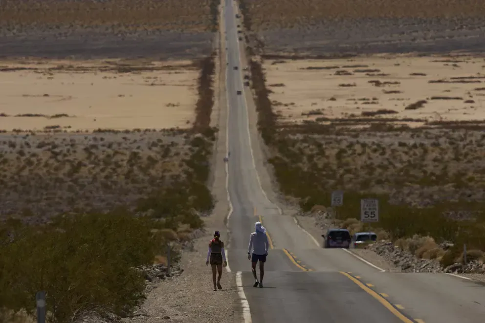 Carretera recta e interminable atravesando el desierto, con dos corredores avanzando bajo el sol hacia el horizonte